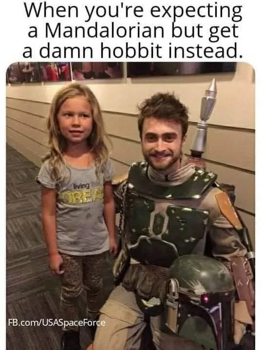 A young girl with blonde hair and a gray t-shirt stands next to a man in full Boba Fett costume, complete with helmet and…