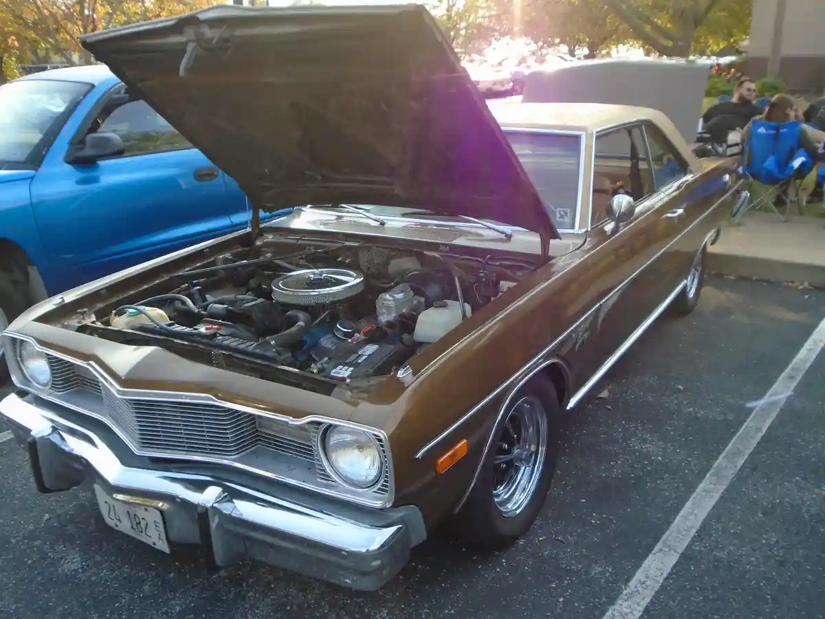 A brown classic American muscle car with its hood open, revealing a detailed engine bay, parked in an asphalt lot with a…