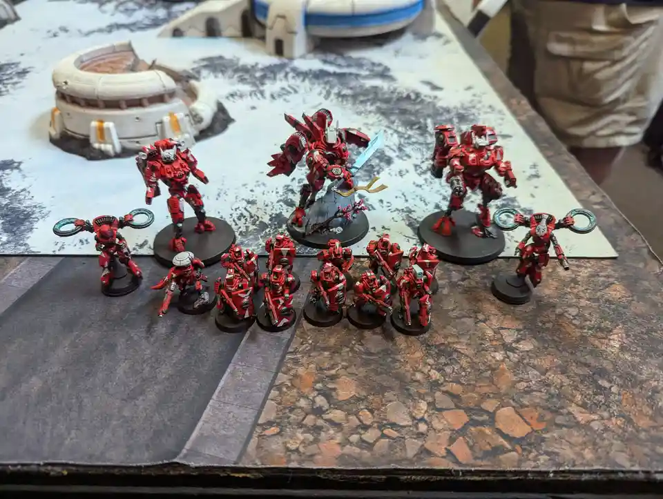 A collection of red-painted miniature robot figures, including one large central figure with a sword and smaller surrounding…