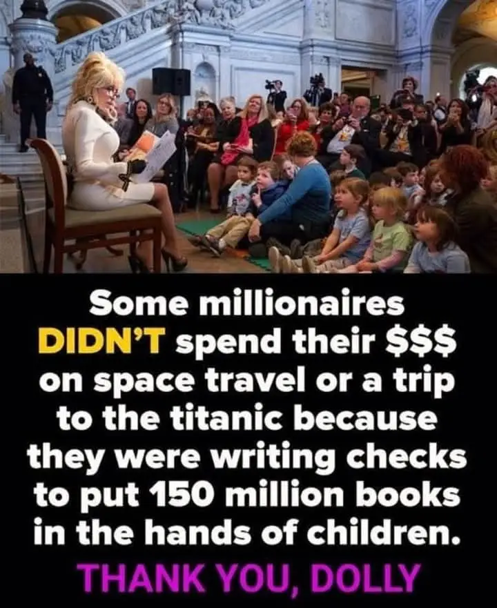 A woman with blonde hair and glasses sits in a chair reading to a group of children in a grand, ornate hall. Behind her…
