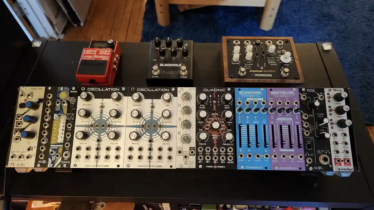 A photo shows a black table with several modular synthesizer modules and guitar pedals. The modules include 'Function'…