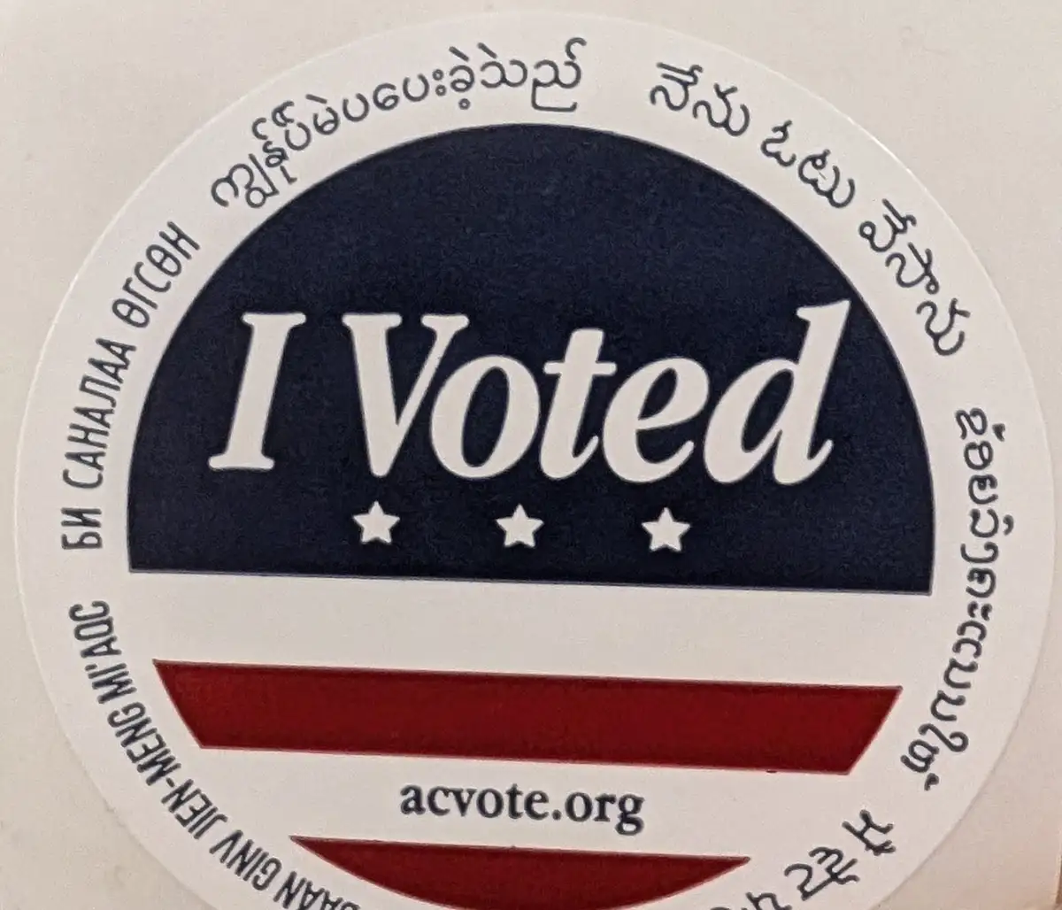 A circular 'I Voted' sticker with a blue upper half and red lower half, featuring three white stars beneath the text. The…