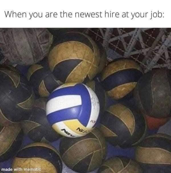A close-up photo shows one bright, clean blue, white, and yellow volleyball sitting prominently among many worn, dirty…