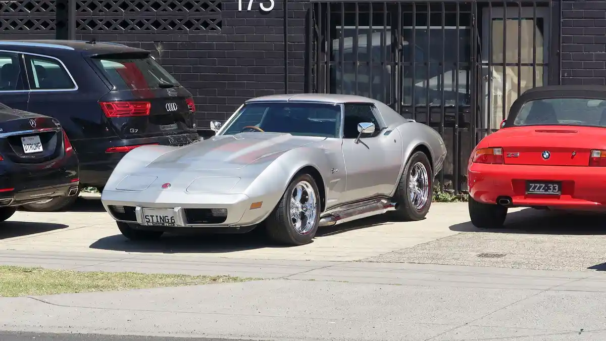 A silver classic Chevrolet Corvette Stingray is parked between a black Audi and a red BMW Z3. The Corvette's license plate…