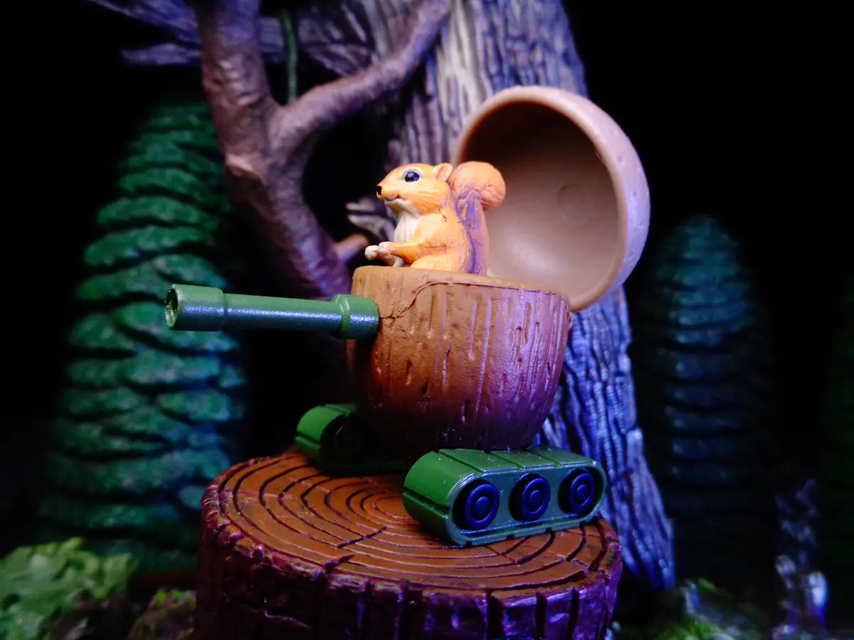 A small orange squirrel figurine sits inside a miniature tank made from a hollowed-out acorn, positioned on a tree stump…