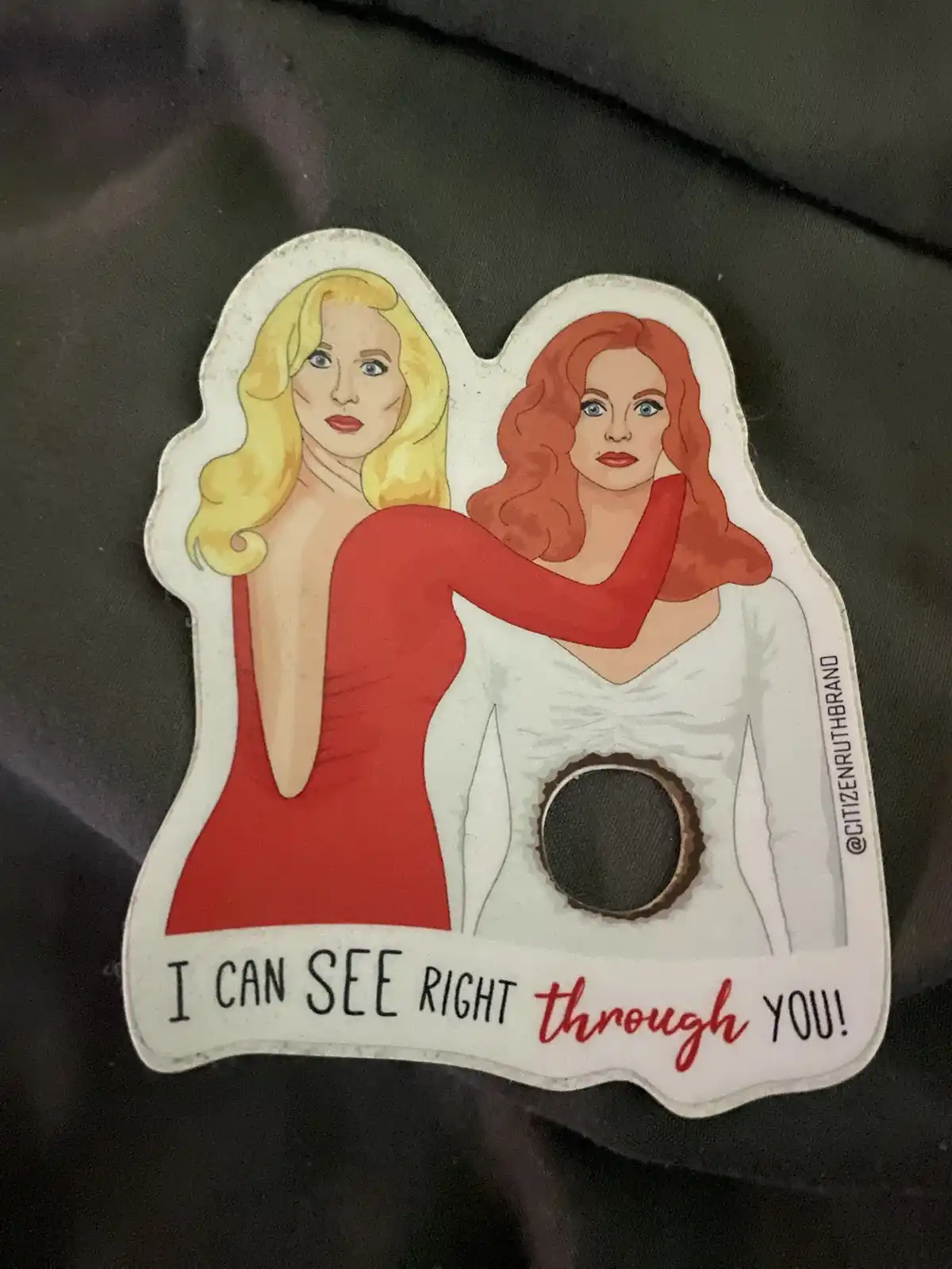 A sticker shows two illustrated women, one blonde in a red dress and one redhead in a white dress with a circular hole…