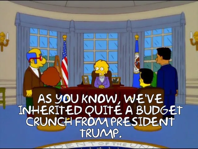 A still from The Simpsons shows President Bart Simpson sitting at a desk in the Oval Office, flanked by two advisors. The…