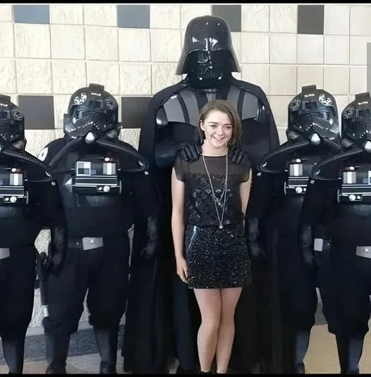 A young woman in a black sequined dress stands smiling in front of Darth Vader and several stormtroopers. The overlaid text…