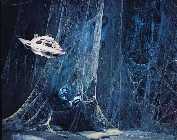 A vintage spaceship is depicted flying through a dense, glowing blue web-like structure that resembles a giant spider's…
