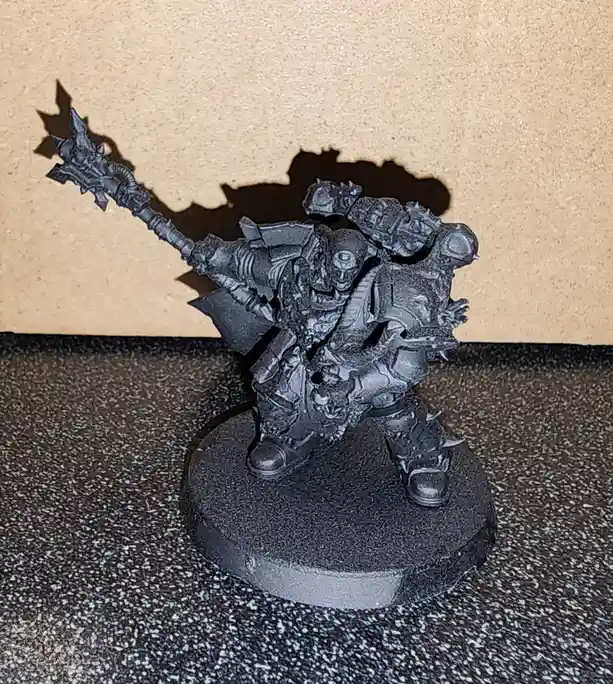A black-painted fantasy miniature of a heavily armored, monstrous warrior wielding a spiked mace stands on a round base. The…