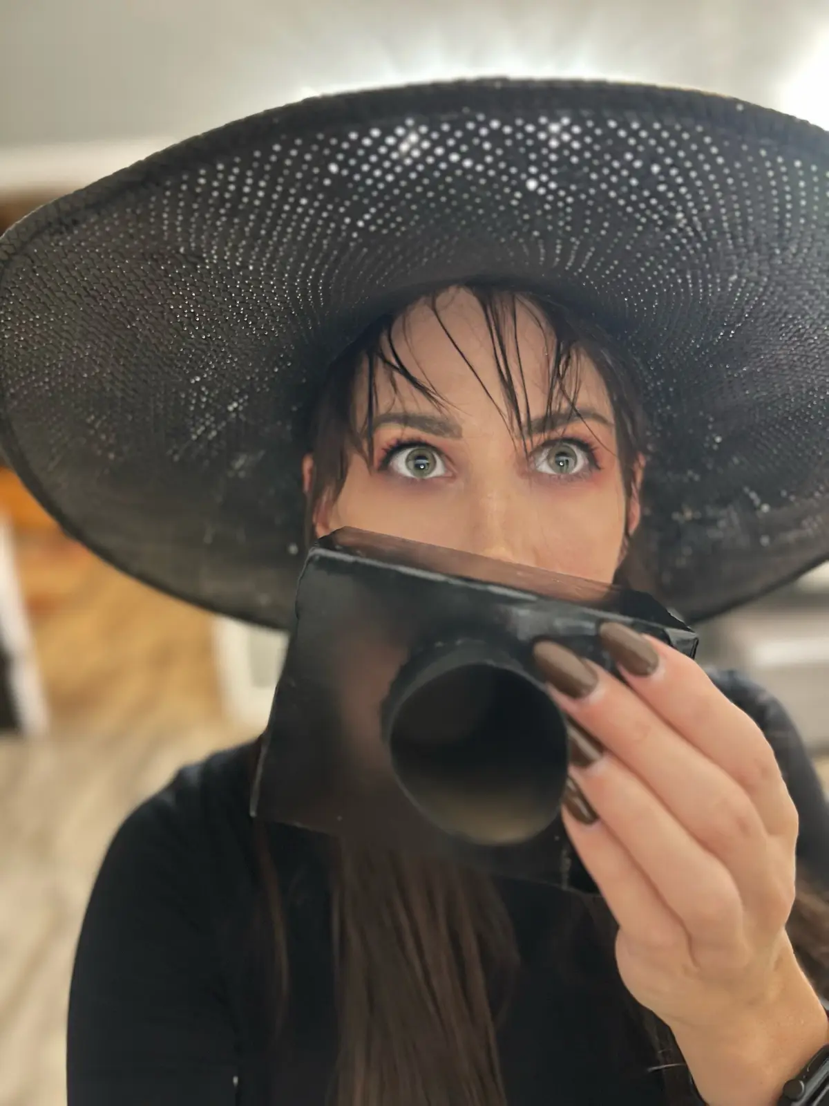 A person with wide, startled eyes peers over the top of a black, rectangular object resembling a camera or pipe, while…
