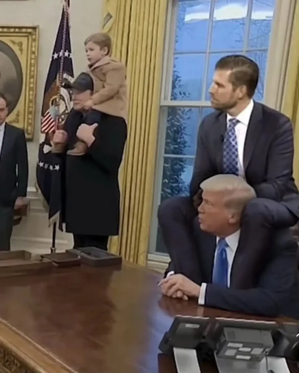 In the Oval Office, a man sits at the desk with his head resting on his arms, while another man stands behind him holding a…