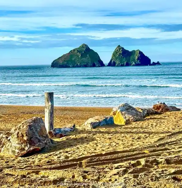 A scenic beach photo shows two large green sea stacks in the distance, waves rolling in, and a sandy foreground with rocks…