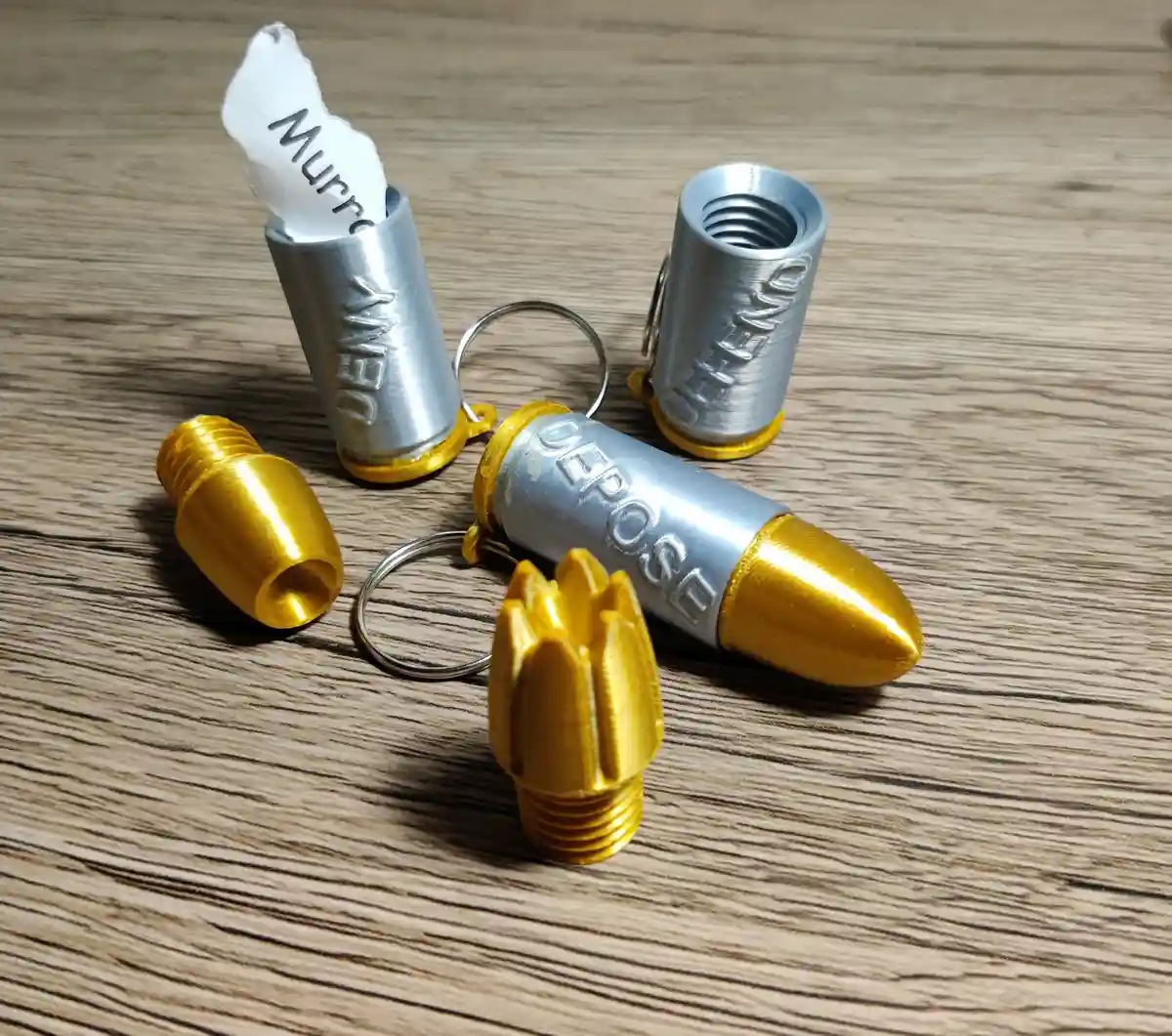 Several 3D-printed bullet-shaped keychains with gold tips and silver casings sit on a wooden surface. One keychain has a…