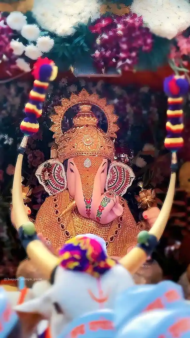 A highly decorated, ornate statue of Lord Ganesha, adorned with gold jewelry, colorful flowers, and intricate patterns, is…