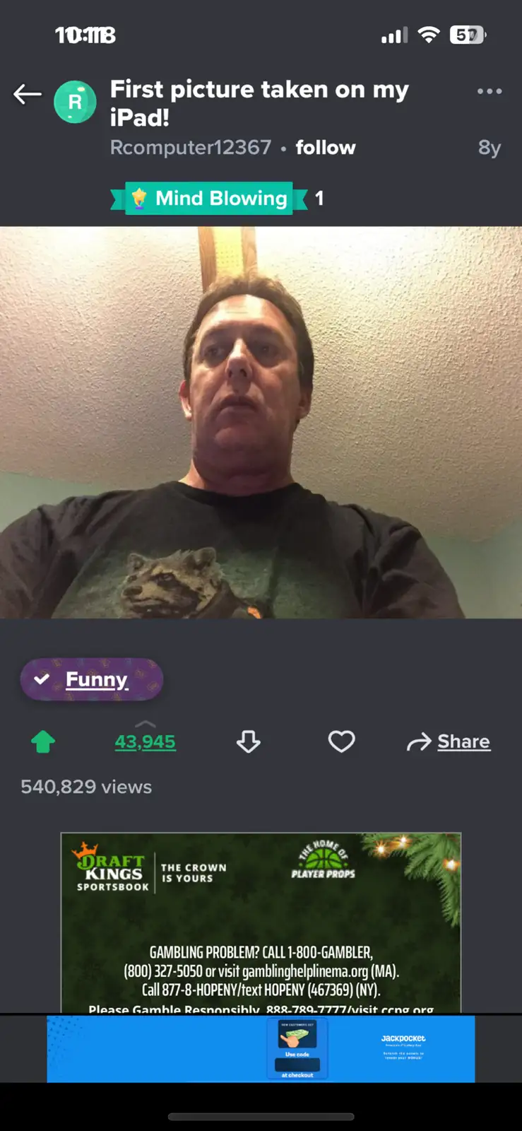 A screenshot of a social media post showing a man in a dark t-shirt with a raccoon graphic, looking upward with a surprised…