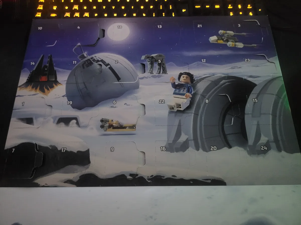 A Lego Star Wars Advent calendar is shown with several doors opened, revealing miniature Star Wars scenes including a…