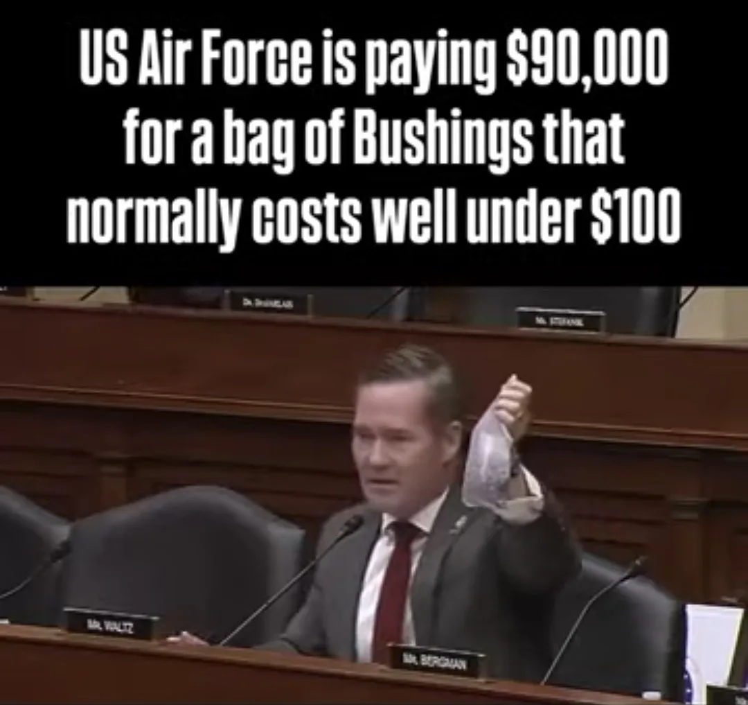 A man in a suit and tie sits at a congressional hearing table, holding up a clear plastic bag containing small mechanical…