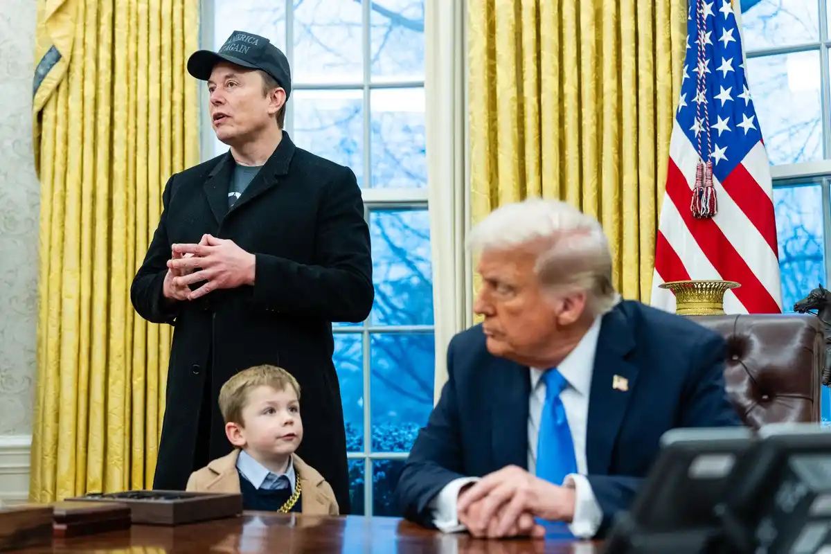 A photo shows Elon Musk wearing a 'Make America Great Again' cap, standing in the Oval Office with a young boy in front of…