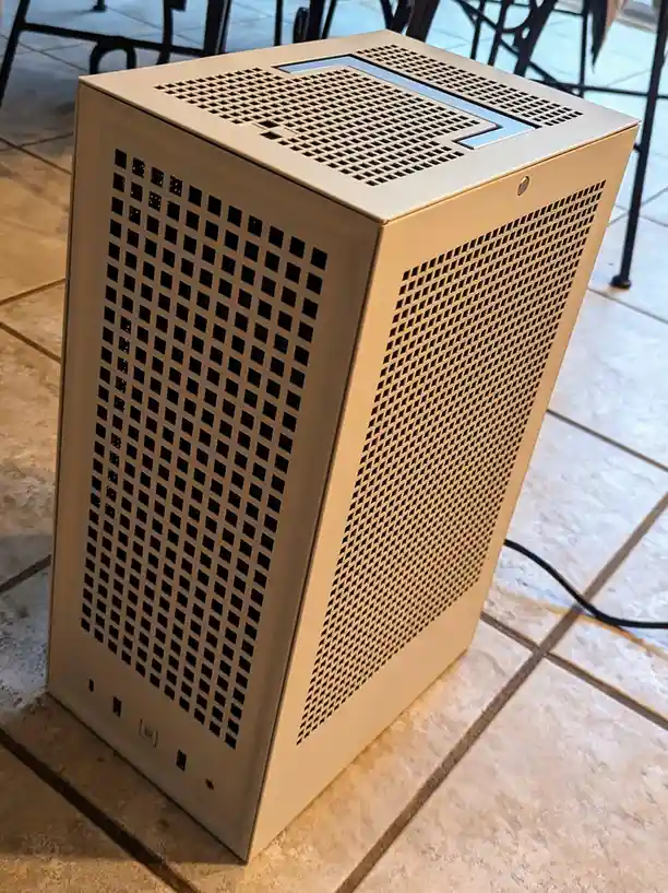 A beige, boxy computer case with perforated ventilation panels sits on a tiled floor, its design resembling a minimalist…