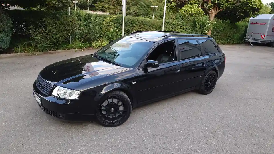 a black audi a4 avant station wagon is parked on asphalt with its driver's door open, featuring black multi-spoke wheels…