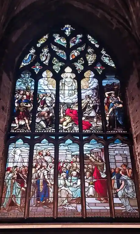 A large, ornate stained glass window depicting multiple biblical scenes with figures in robes, set within a stone arch…