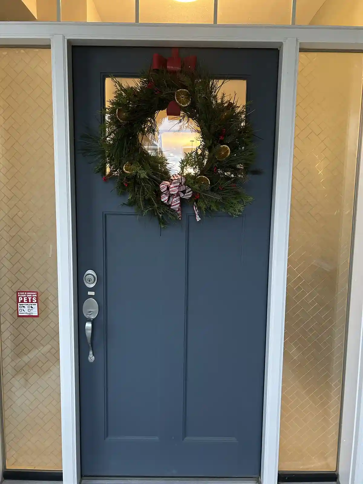 A blue front door with a festive green wreath adorned with red berries, dried orange slices, and red and white bows. On the…