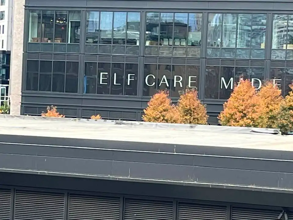 A photo of a modern building's glass facade with the words 'ELF CARE MADE' visible in white lettering. In front of the…