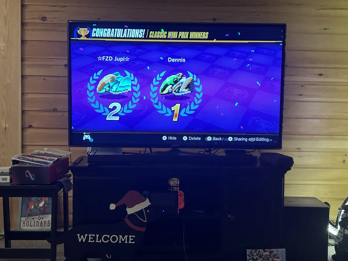 A television screen displays a video game race results screen with 'CONGRATULATIONS! | CLASSIC MINI PRIX WINNERS' at the…