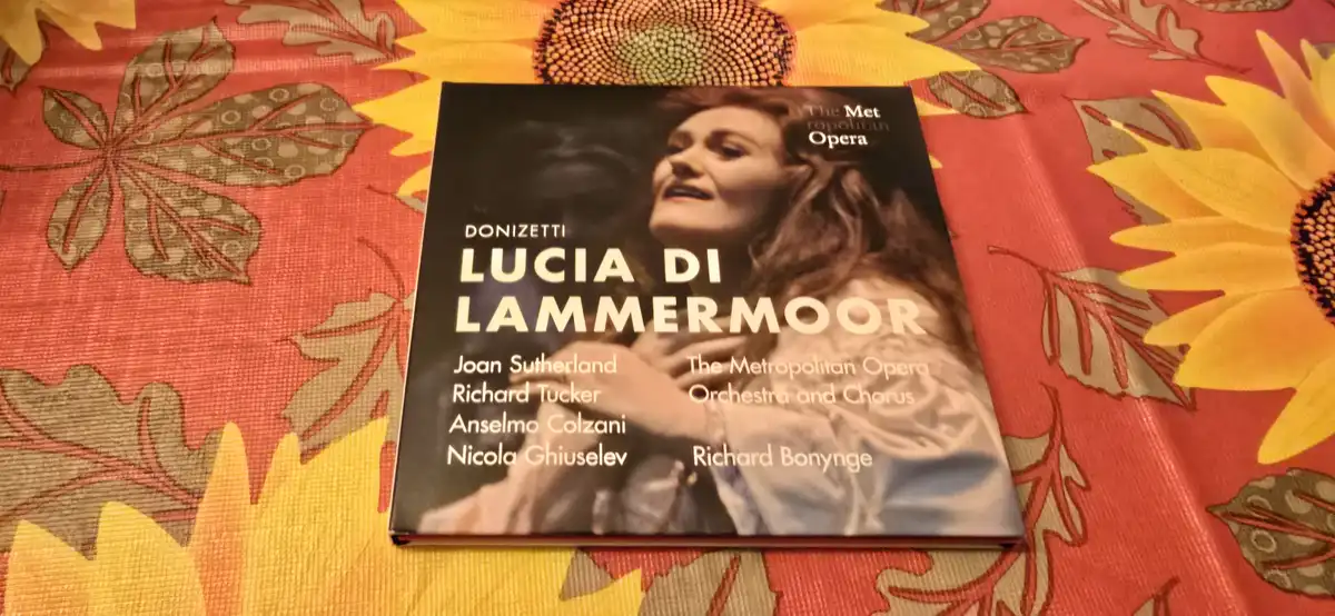 A physical copy of the opera 'Lucia di Lammermoor' by Donizetti, featuring Joan Sutherland, is placed on a bright red and…