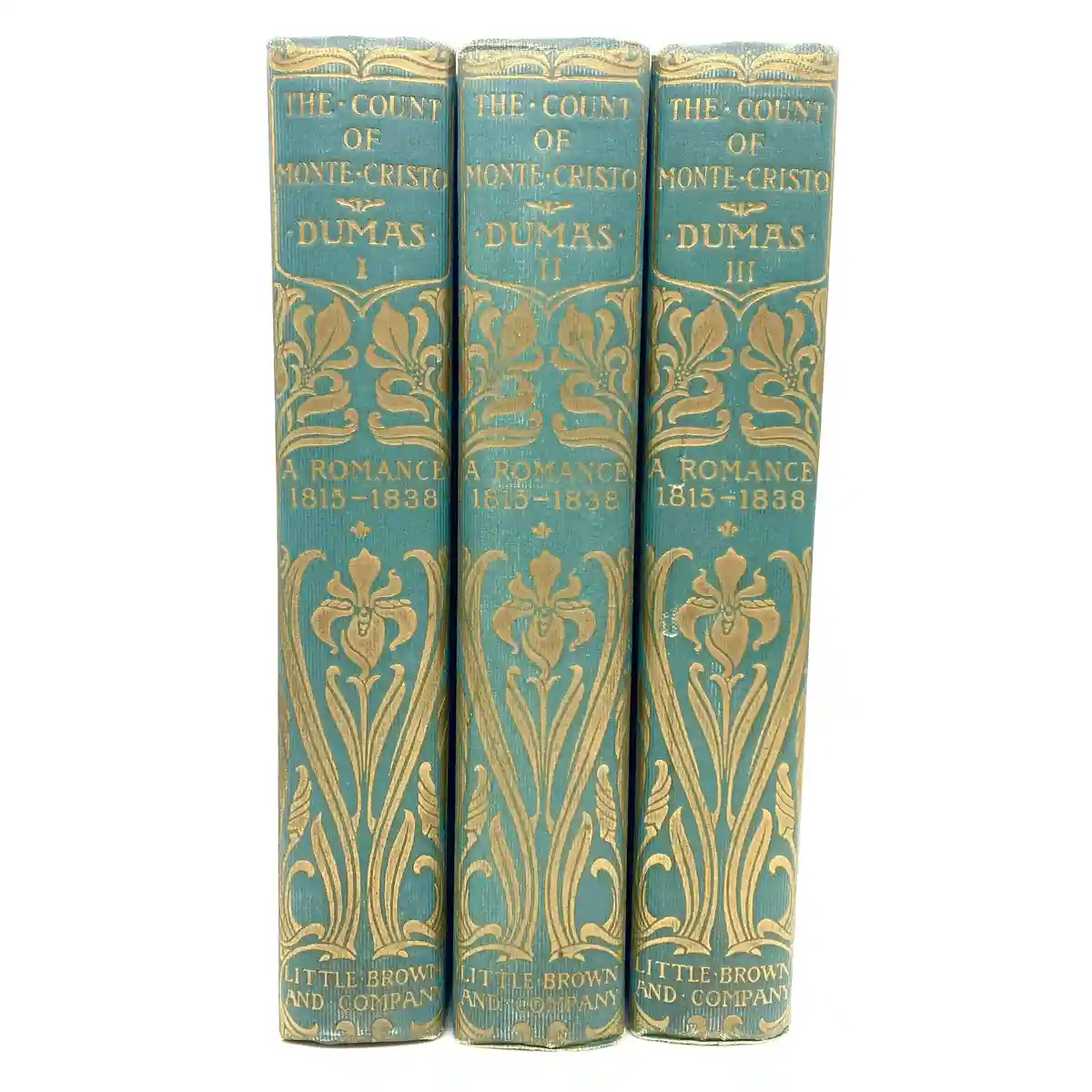 Three vintage blue hardcover books standing upright, each labeled 'THE COUNT OF MONTE CRISTO' by 'DUMAS' with Roman numerals…