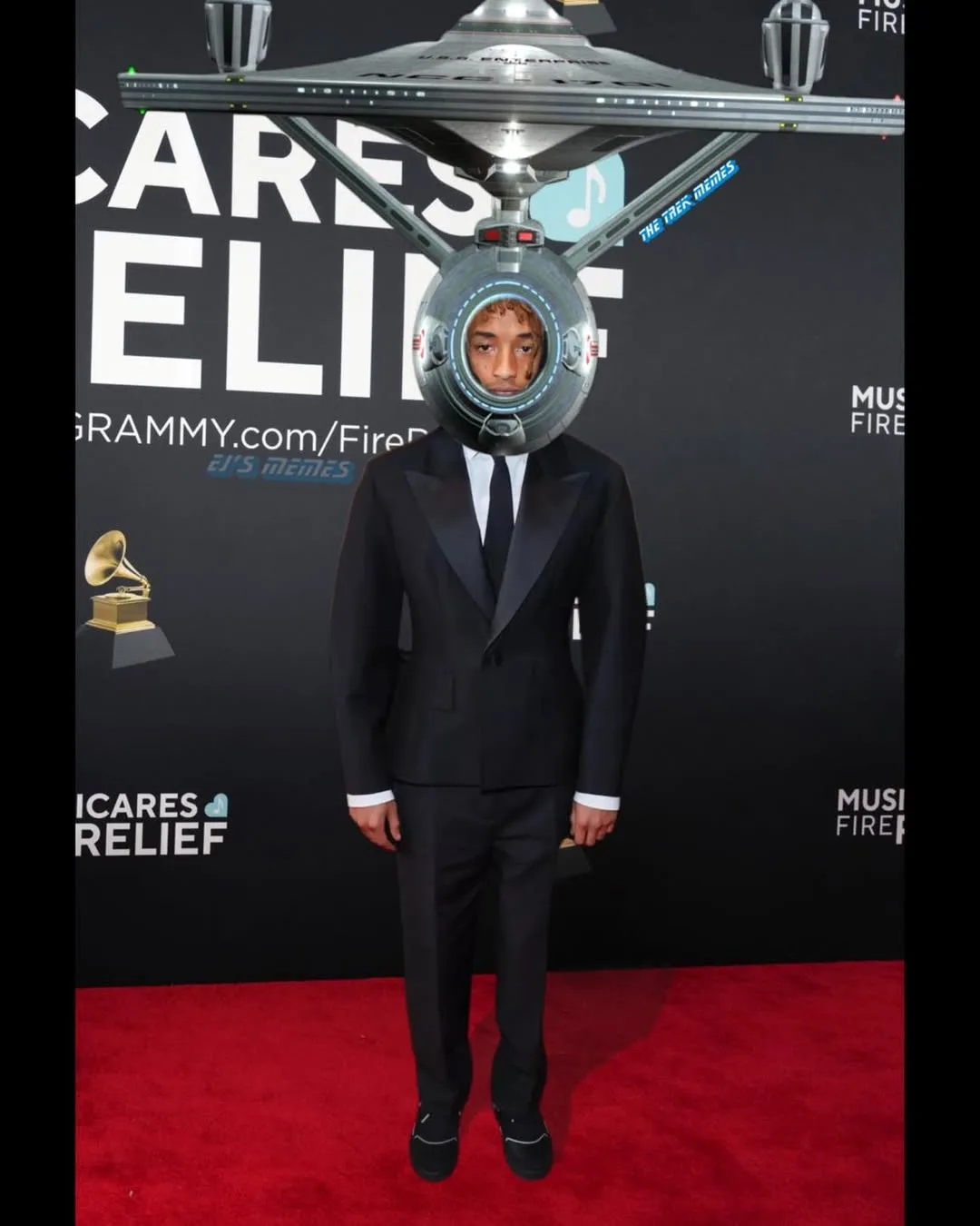 A man in a black tuxedo stands on a red carpet at a Grammys event, with a Star Trek Enterprise spaceship digitally…