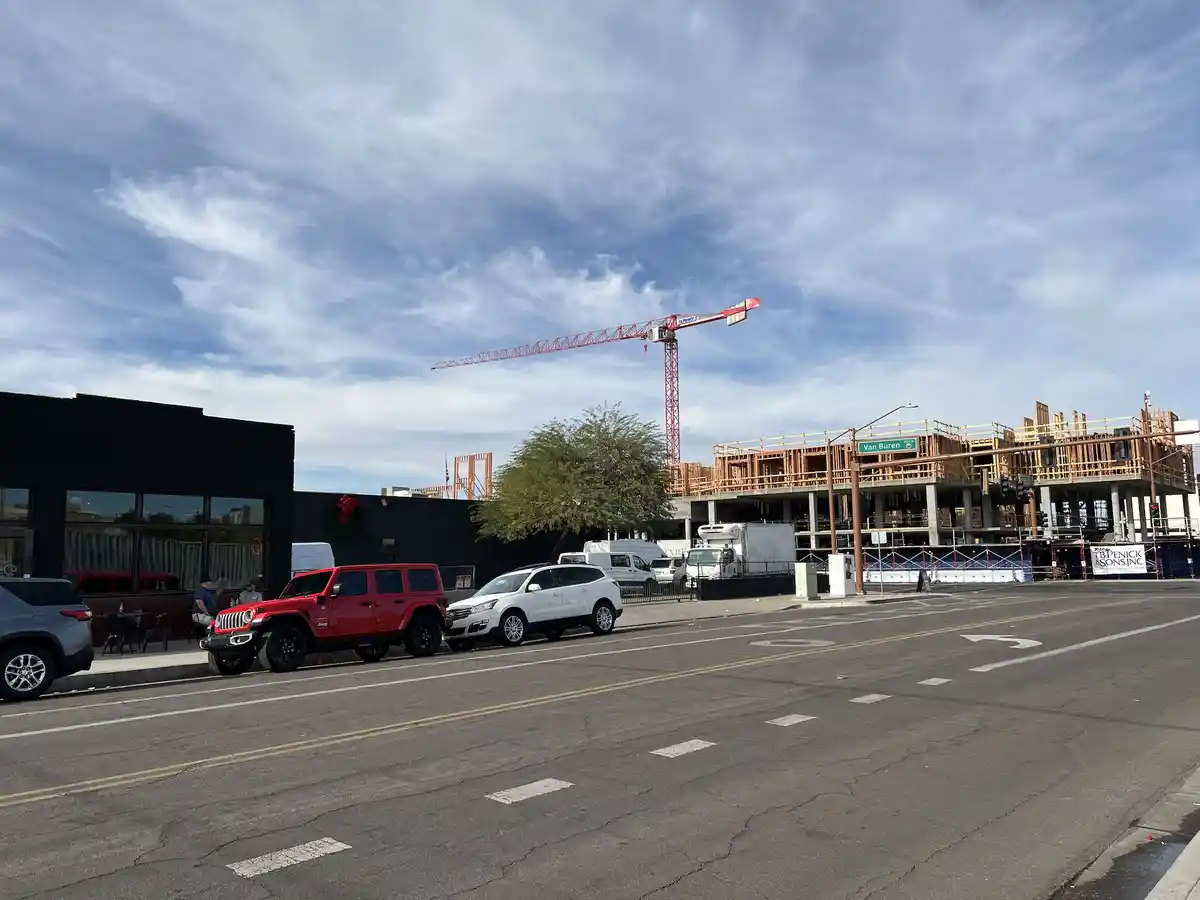 A street view shows a red Jeep parked next to a white SUV, with a large red construction crane and a partially built…