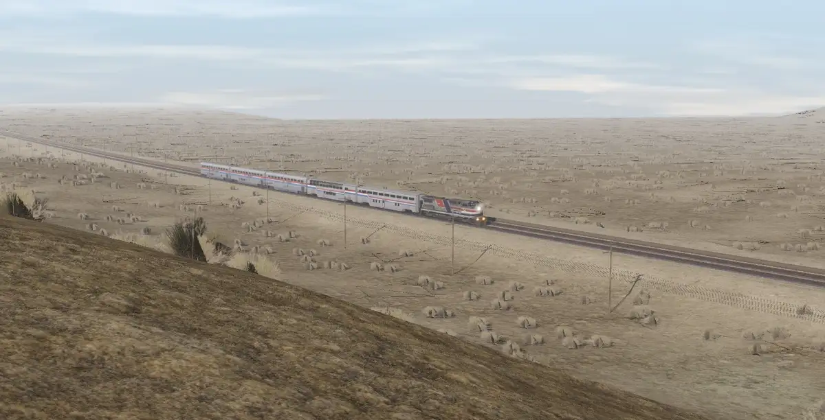 A long passenger train travels through a vast, arid, and sparsely vegetated desert landscape under a pale sky. The train…