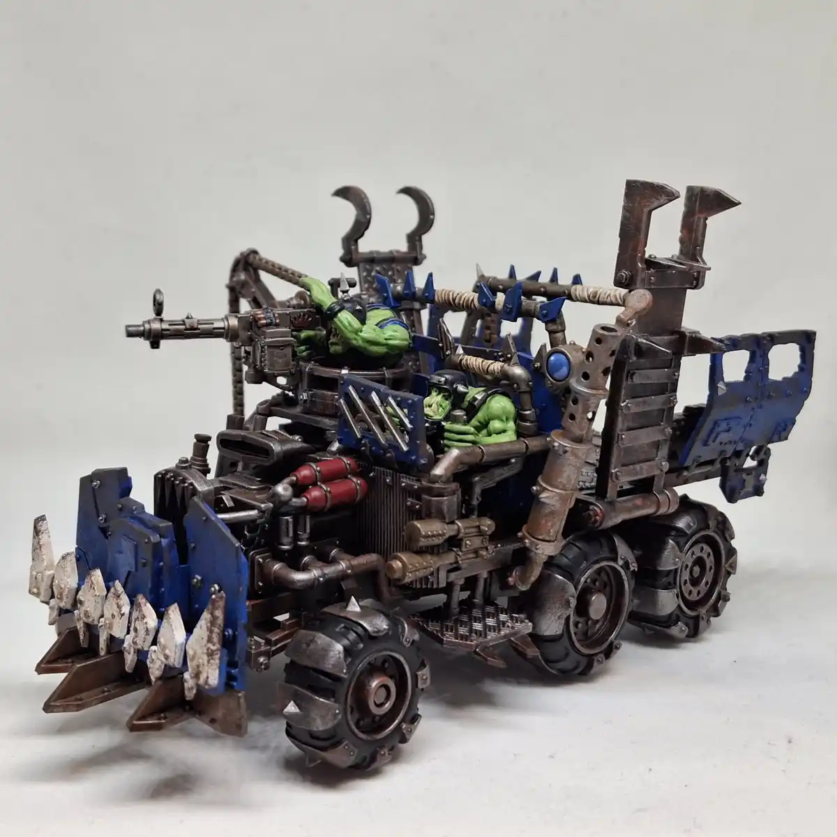 A heavily modified, rusted, and spiked green orc war vehicle with two orc figures inside, one operating a large gun and the…