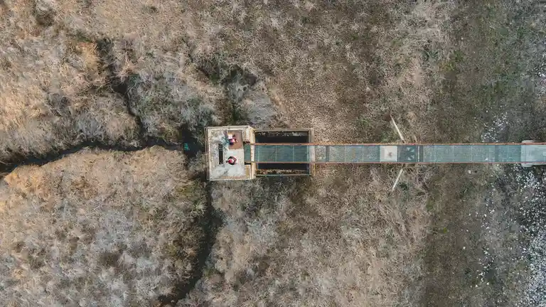 A lone bridge stretches across the desolate expanse, a fragile thread connecting two distant points amidst a vast, rocky…