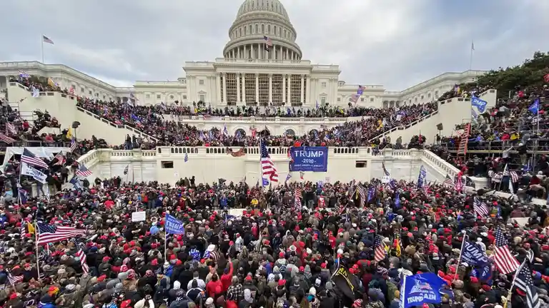 A large crowd of people wearing red hats and holding American flags and signs gathers on the steps of the U.S. Capitol…