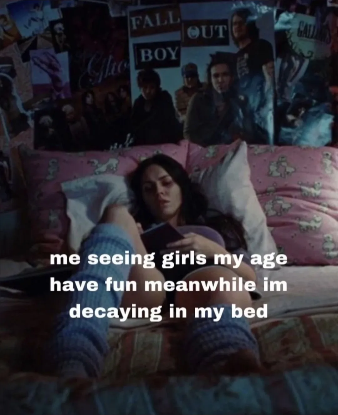 A young woman lies in bed surrounded by posters, notably Fall Out Boy, looking bored while holding a phone. The overlaid…