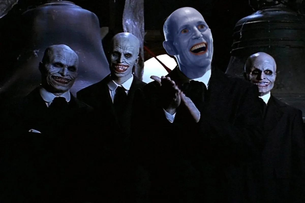 Four pale, bald men in black suits with exaggerated, sinister grins stand in a dimly lit setting with large bells behind…