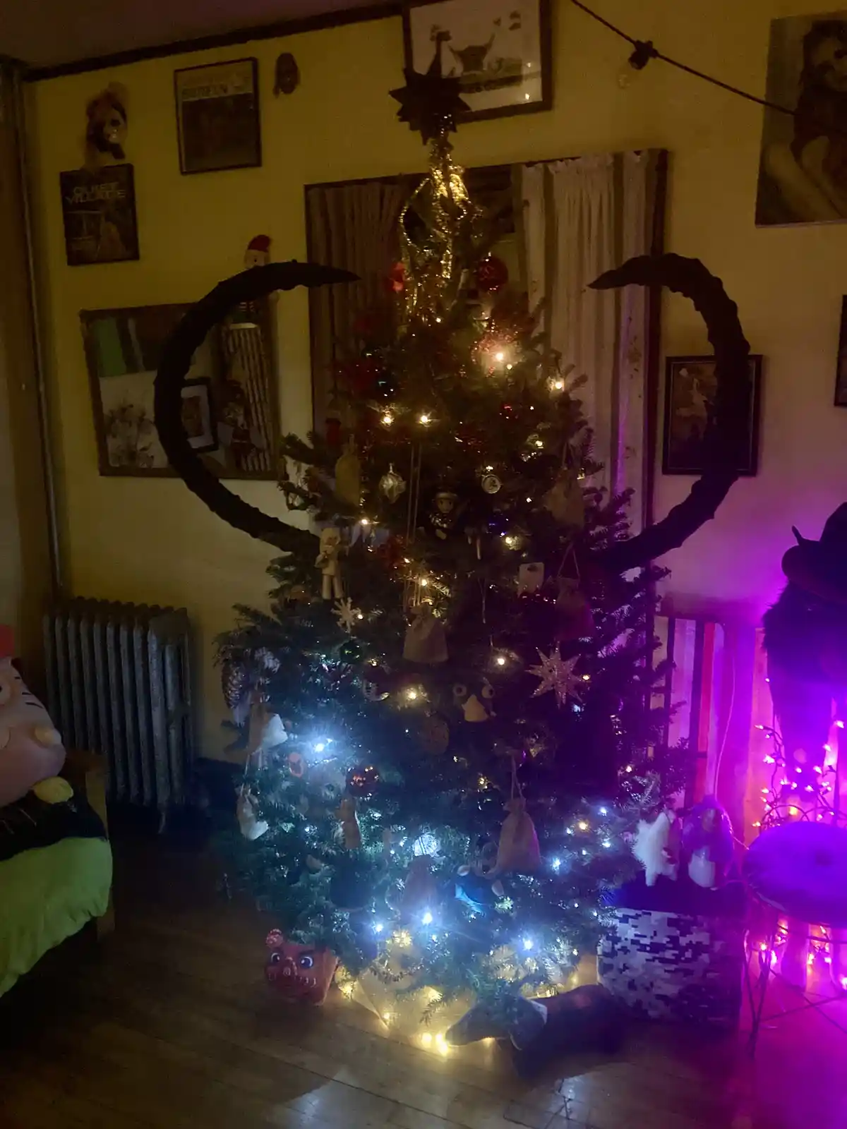 A decorated christmas tree with lights and ornaments is digitally edited to have large, curved black horns protruding from…