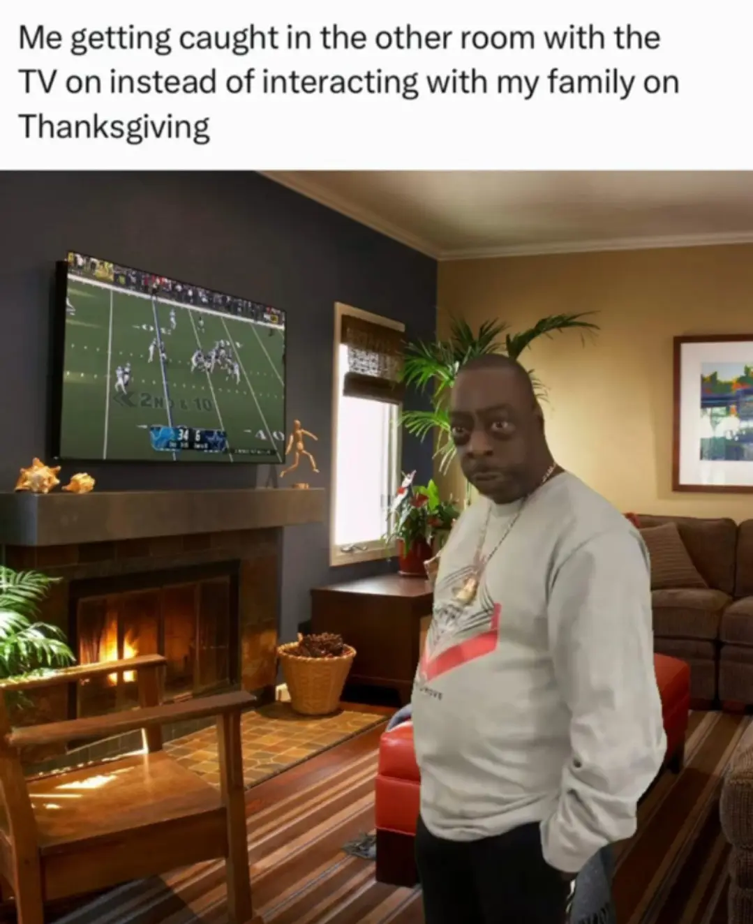 A man stands in a living room with a surprised or guilty expression, looking toward the camera. Behind him, a large TV…