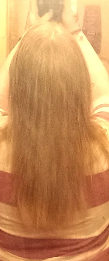 A blurry, low-resolution photo shows the back of a person with long, straight, light-brown hair, wearing a horizontally…