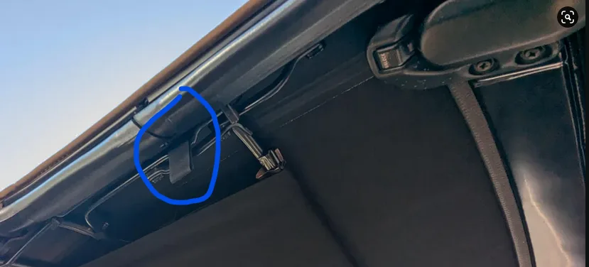a close-up photo of a car's interior roofline, showing a black sun visor mechanism with a blue circle highlighting a small…
