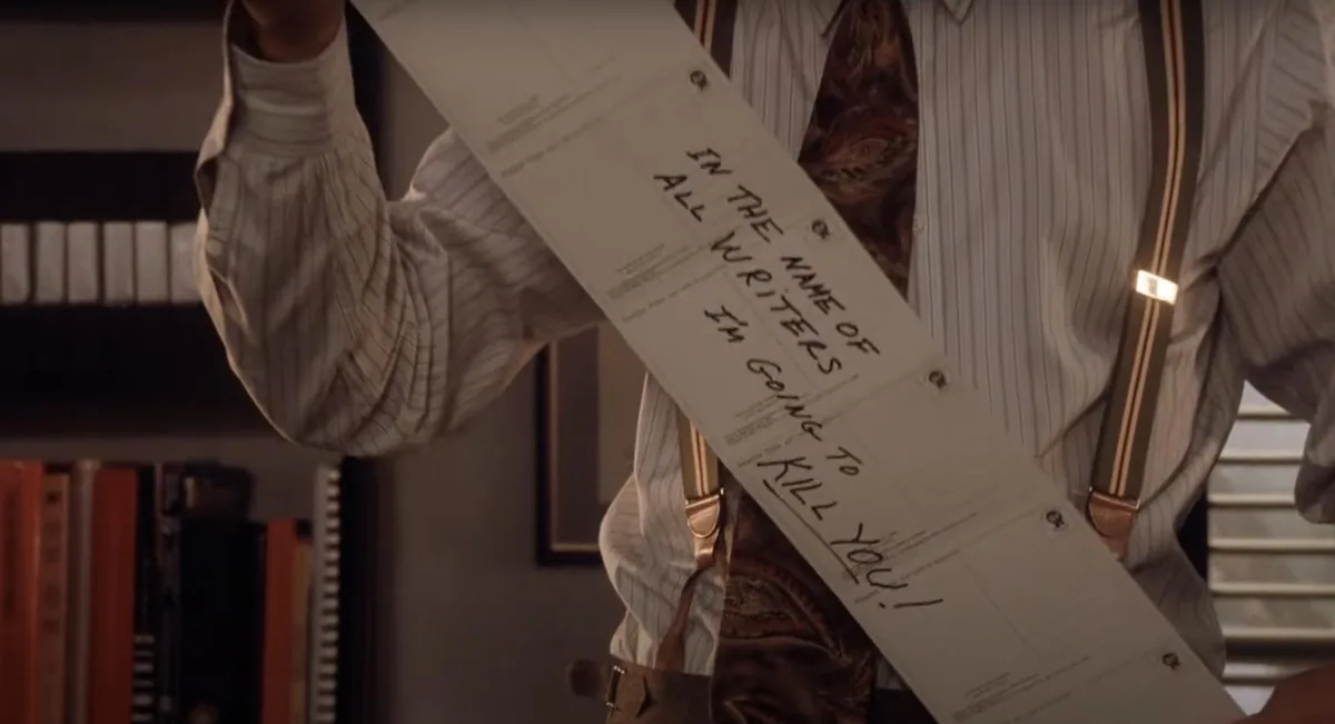 A person in a striped shirt and suspenders holds up a long document with handwritten text that reads 'IN THE NAME OF ALL…