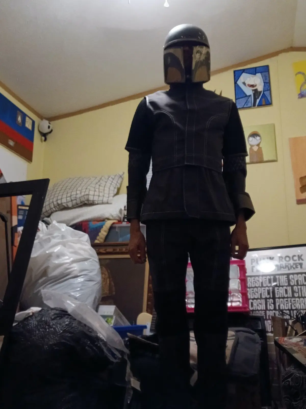 A person stands in a cluttered room wearing a full Mandalorian costume from 'The Mandalorian' TV series, including the…