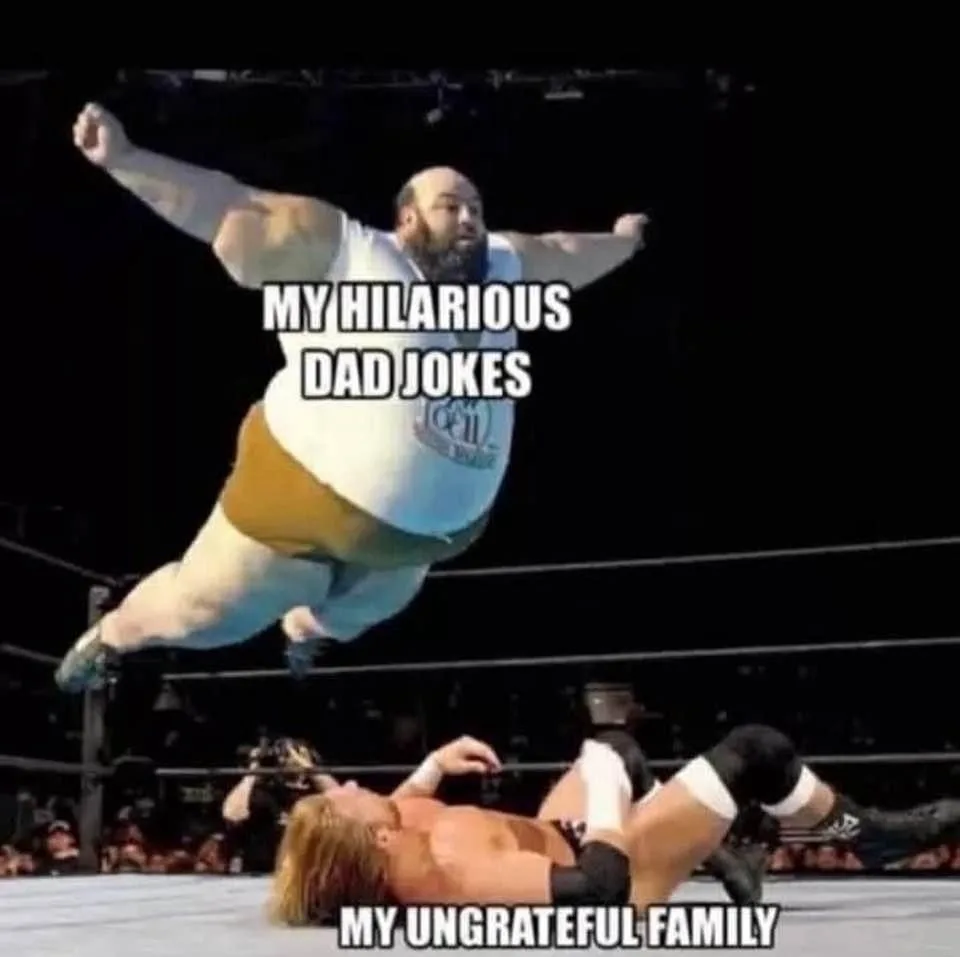A large, bearded wrestler in a white tank top and tan trunks leaps mid-air toward another wrestler lying on his back in a…