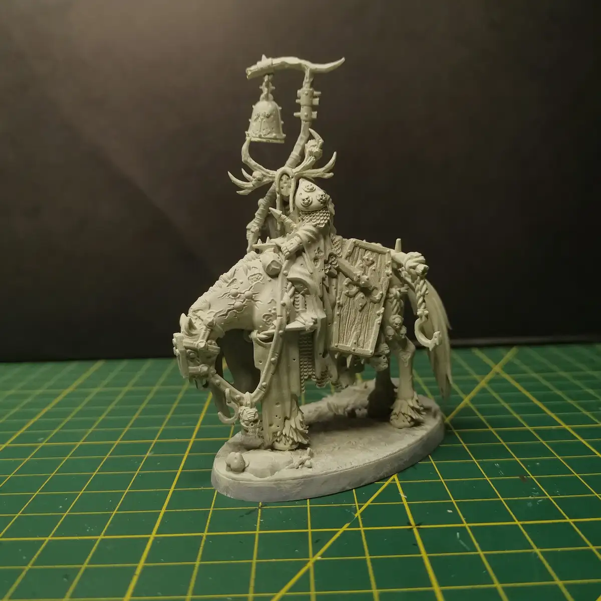 A highly detailed, unpainted white miniature of a fantasy warrior on a skeletal horse, holding a large ornate weapon with a…