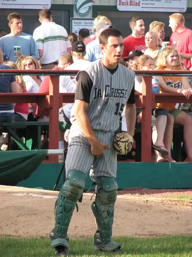 A baseball player in a gray pinstripe uniform with 'JA CROSSE' and number 15 on the chest, wearing catcher's gear including…