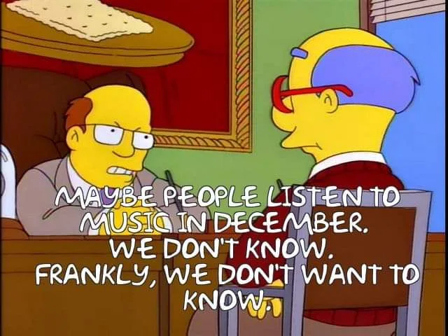 Two Simpsons characters sit across a desk from each other. The character on the left, wearing glasses and a suit, looks…