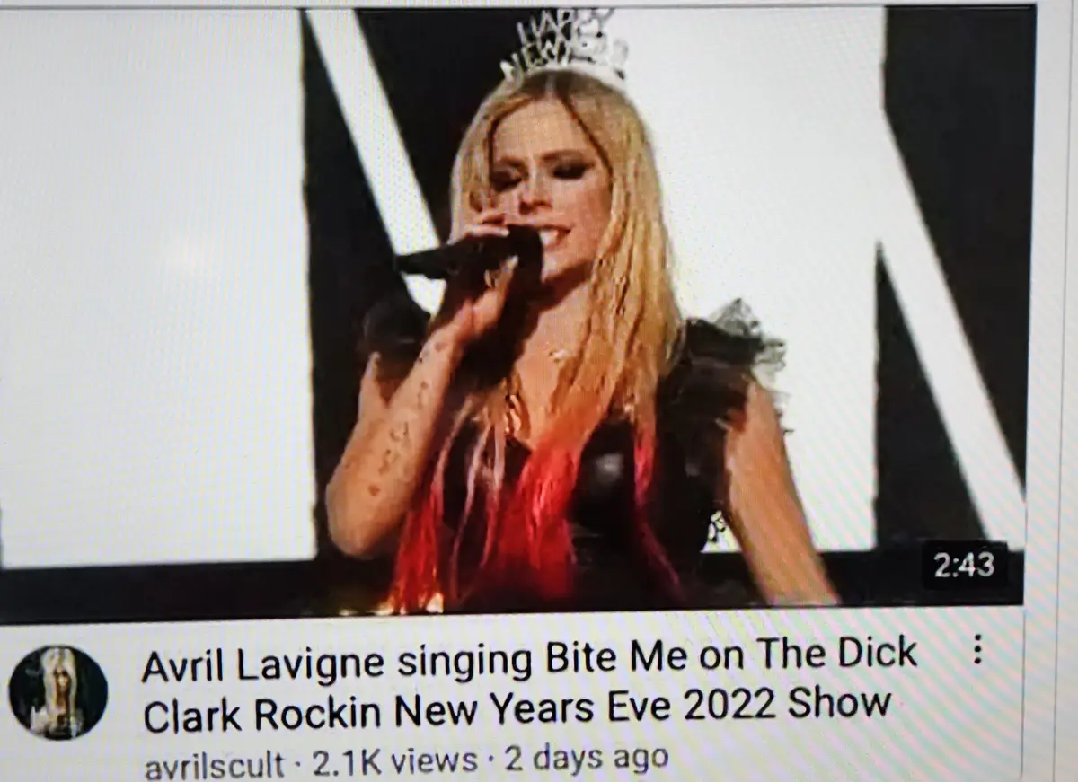 A screenshot of a YouTube video thumbnail shows Avril Lavigne performing on stage, wearing a tiara and holding a microphone…